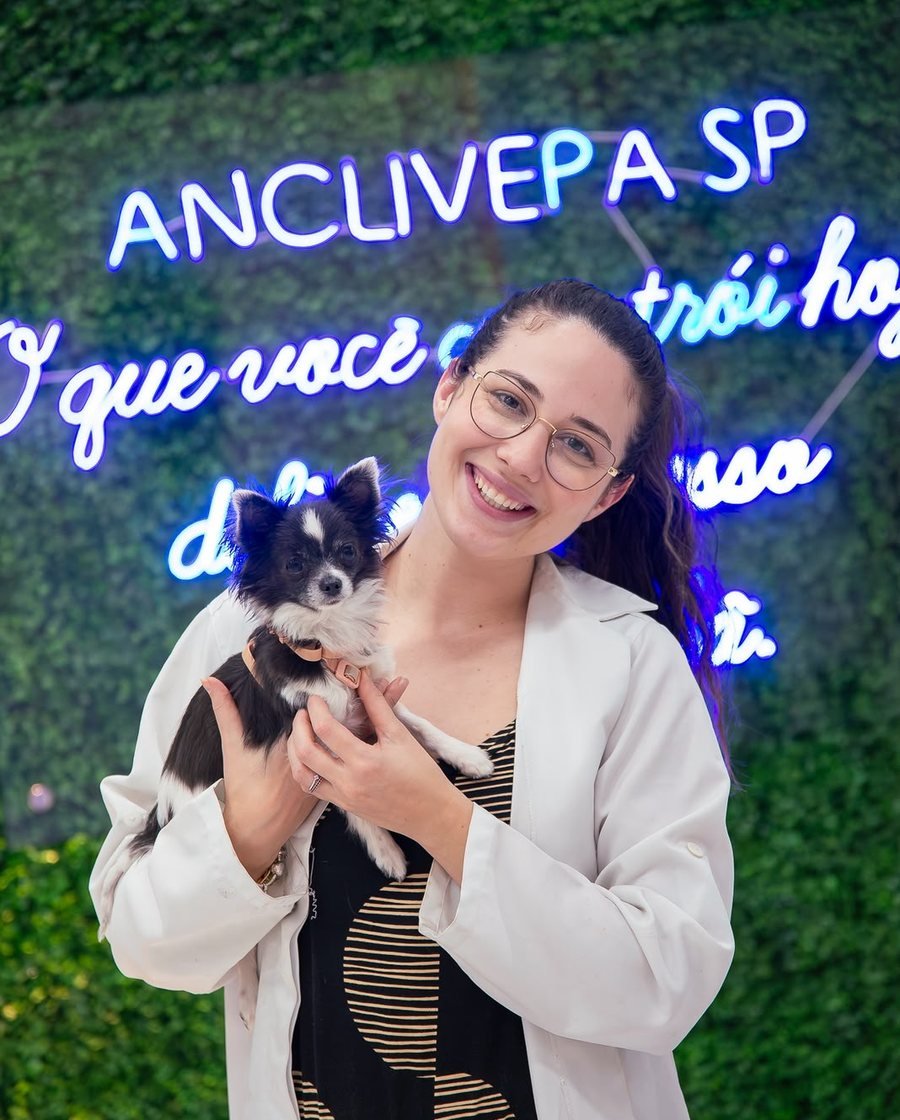 Dra. Heloisa Minotti de jaleco, segurando um cão de pequeno porte